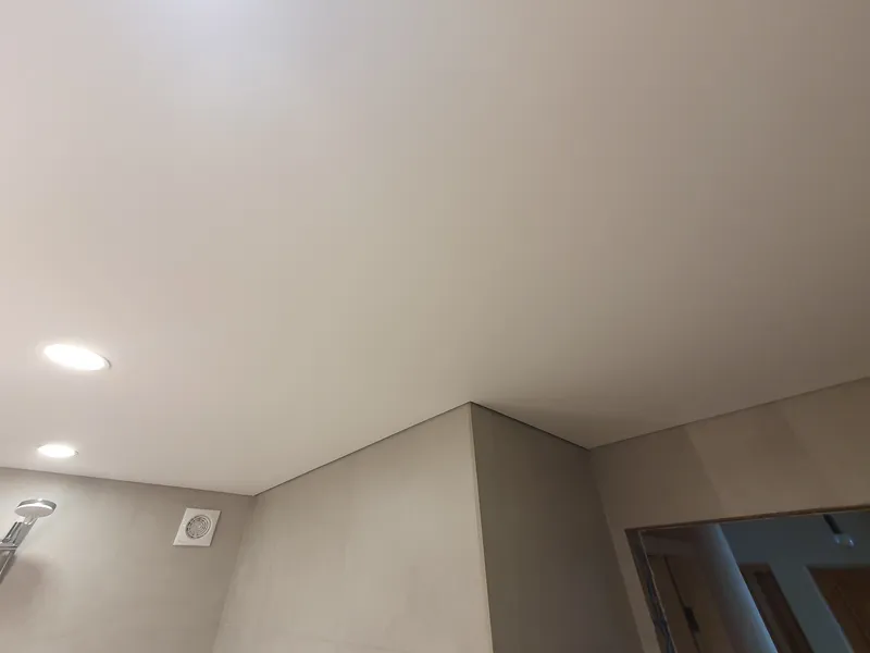 Stieptie griesti ar iebūvētiem gaismekļiem, ventilācijas reste un dušas statne pie flīzētās sienas.