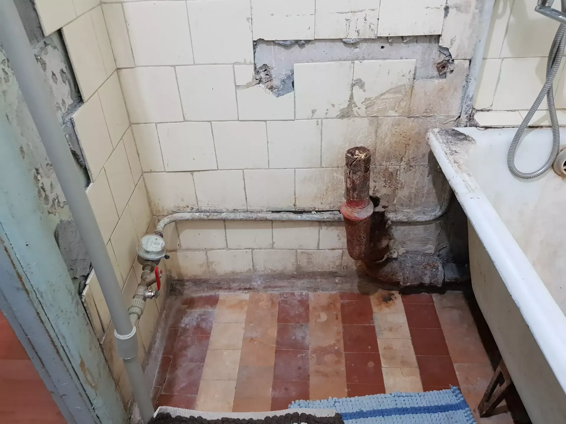 До ремонта: старая ванна, чугунная канализация и водяной счётчик у стены.