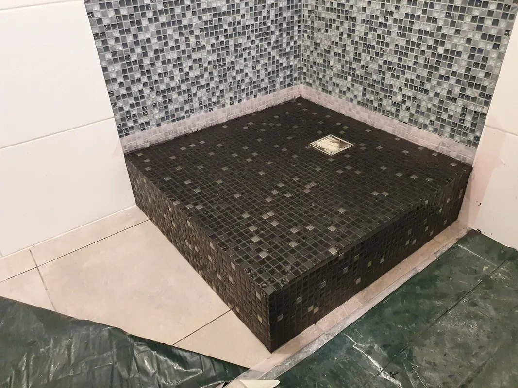 Готовый подиум под душ, облицованный тёмной мозаикой, решётка трапа в центре — вместо старого поддона.