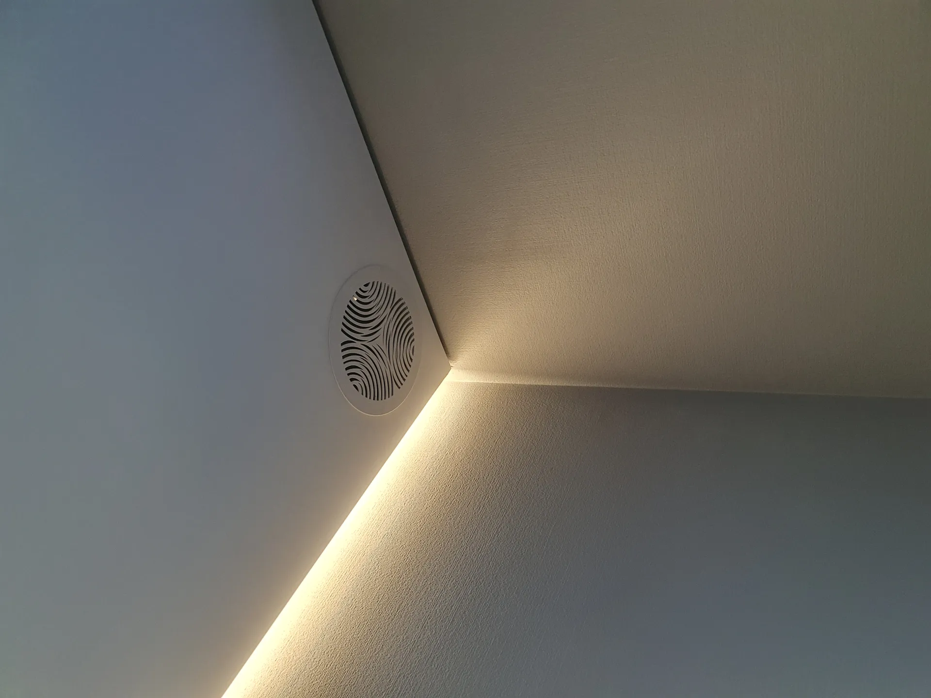 Угол потолка: LED-линия по краю натяжного потолка и круглая вентиляционная решётка.